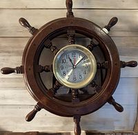 Front view of wood ship's wheel with brass-framed clock
