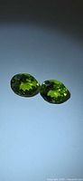 Pair of faceted oval peridot gemstones on light surface