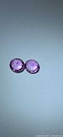 Two round faceted hot pink gemstones side by side on neutral background
