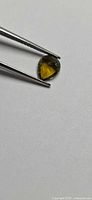 Pear-shaped green yellow gemstone held by tweezers