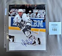 Full view of signed 8x10 photo in plastic sleeve with MaxSold lot card