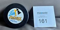 Front of puck showing Penguins logo, autograph and hand numbering 302/500 beside MaxSold lot card
