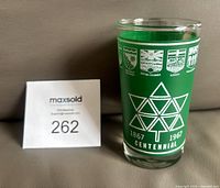 Front view of glass displaying maple-leaf centennial logo, provincial shields, height reference card