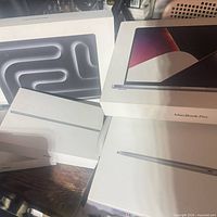 Stack of Apple product boxes: visible MacBook Pro, MacBook Air, iPad boxes