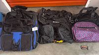 Three duffle bags lined up: large black/blue, Sony black, purple patterned