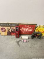 All items arranged: two wooden signs, yellow round tin sign, bottle opener, green bench display, die-cast car with packaging