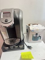 Front view of Keurig coffee maker on pod drawer beside boxed rice cooker