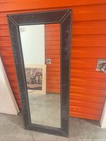 Front view of rectangular mirror with black stitched frame leaning against wall