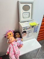 Overall lot showing boxed Philips Avent sterilizer, three baby dolls, and Jesus Loves Me photo frame