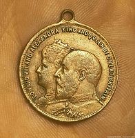 Front of metal coronation medallion showing portraits and inscription