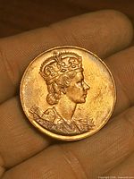 Obverse shows crowned left-facing portrait of Queen Elizabeth II on copper medallion held in hand for scale