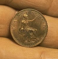 Close-up of 1933 farthing coin on finger, showing reverse