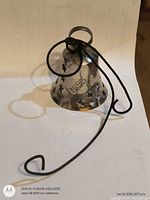 Side view of silver-plated bell showing USPS imprint and star cutouts with cord visible