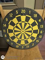 Front view of yellow and black wooden dartboard showing numbers and center bullseye