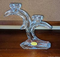 Front view of clear crystal double-arm candle holder showing sweeping curved design and base label
