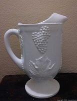 Side view of footed milk glass pitcher showing grape motif and handle