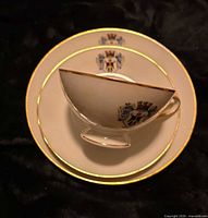 Cup stacked on saucer and plate showing gold trim and crest