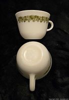 Two Pyrex Spring Blossom Green cups, one upright, one inverted to show pattern and handle