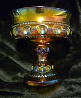 Side profile of amber iridescent crown-pattern compote on dark fabric