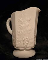 Side view of milk glass creamer showing Paneled Grape pattern and pedestal base