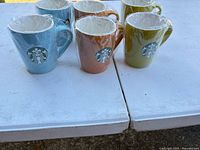Six Starbucks mugs individually plastic-wrapped on table