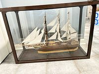 Front view of model ship inside wooden-framed glass case