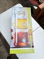 Retail box showing image of stacked glass beverage dispenser with lid and two spouts