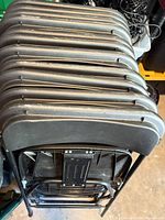 Stack of 11 black folding chairs viewed from top showing backs and frames