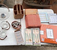 Overview of entire lot on table including bowls, tablecloth, cutlery packs, binder, napkin rings, teaspoons and pewter figurines