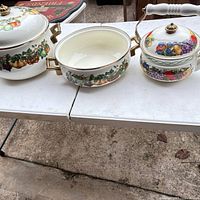 Three enameled cookware pieces on table showing decoration and sizes