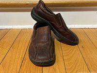 Pair of brown slip-on shoes side view, one shoe propped on the other