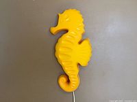 Front view of yellow seahorse wall lamp, cord visible