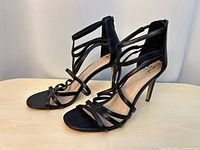 Side view of both black strappy high-heel sandals showing multi-strap design and toe shape