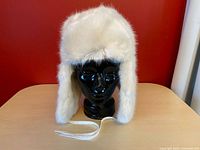 Front view of white faux fur trapper hat on mannequin head showing ear flaps and ties