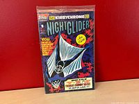 Front of factory-sealed Night Glider #1 comic with visible card area