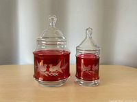 Two cranberry flash etched glass apothecary jars with lids side by side