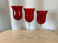 Front view of three graduated ruby-red glass candle holders on clear stems