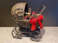 Side view of wicker baby carriage showing wheels, hood, red bow