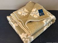 Folded olive and cream floral wool blanket showing whip-stitched edge