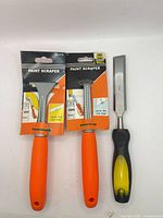 Front view showing two packaged Grip Well paint scrapers and one 25 mm chisel