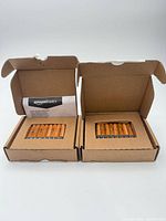 Two open Amazon cardboard boxes showing 8 orange AAA batteries in each