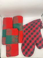 Three red and green Christmas tea towels rolled next to red and black plaid oven mitt