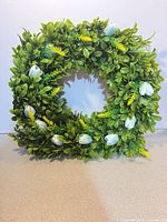 front view of green boxwood wreath with blue buds and yellow fern accents