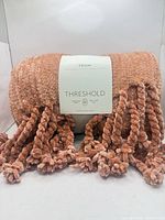 Front view of rolled throw blanket showing brand tag and tassels