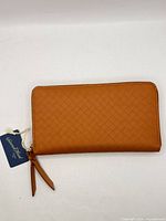 Front view of tan woven-pattern wallet with wristlet strap and tag