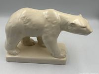 Left side view of cream-white ceramic polar bear on plinth base
