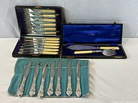 All three groups of flatware displayed: Sheffield boxed set open, Ellis Bros. servers boxed, seven ornate knives on cloth roll