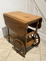Full view of wooden drop-leaf tea cart with one leaf down, showing shelves, wheels, and casters