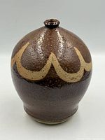 Front view of brown glazed stoneware bud vase with tan wave design