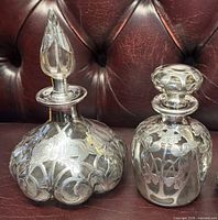 Two Gorham sterling silver overlay glass perfume bottles on leather surface
